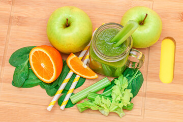 Fresh Green Smoothie of Apple, Celery, Spinach and Orange in Glass Smoothie Jar with Yellow Cocktail Straw on Wooden Cutting Board. Vegan Detox Drink. Vegetarian Culture. Healthy Eating and Fruit Diet