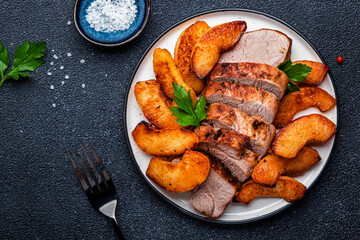 Fried pork tenderloin with quince or apple slices served on plate. Black table background, top view