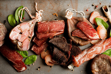Various smoked and cured meat snacks over concrete table background. Cured meat, dry sausage, salceson with seasonings - charcuterie plate, traditional craft antipasti
