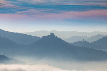 Obraz premium Herbstliches Panorama vom Pfälzerwald mit Berggipfeln und Tälern im Nebel. In der Bildmitte sieht man die Burg Trifels bei Annweiler