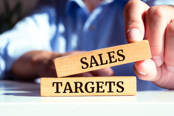 Closeup on businessman holding a wooden blocks with text SALES TARGETS, business concept