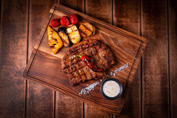 juicy steak with vegetables and sauce on a wooden board on a wooden background