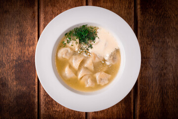 dumplings with broth and sour cream on a wooden background