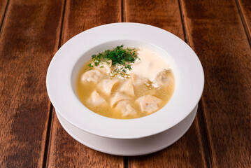 dumplings with broth and sour cream on a wooden background