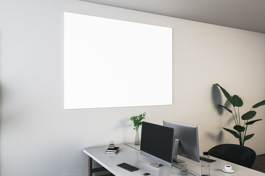 Perspective view on blank white poster with space for your logo or text on light wall background above light work table with modern computers and office tools. 3D rendering, mockup