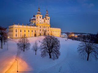 Fototapeta na wymiar Aerial, evening view of the Pilgrimage church of Minor Basilica of the Visitation of the Blessed Virgin Mary illuminated by lamps, covered with snow. Orange and blue colors. Christmas holidays in Czec
