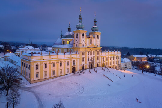 Aerial, winter evening view of the pilgrimage church of the Minor Basilica of the Visitation of the Virgin Mary covered with snow. Pastel colors, snow falling, people celebrate Christmas holidays.