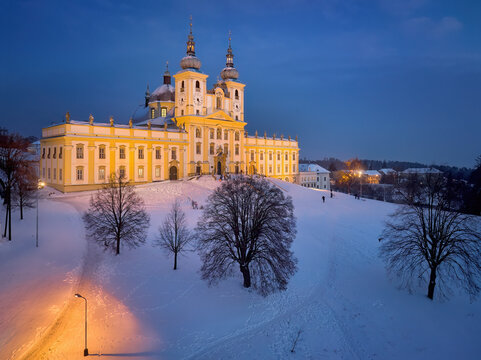 Aerial, evening view of the Pilgrimage church of Minor Basilica of the Visitation of the Blessed Virgin Mary illuminated by lamps, covered with snow. Orange and blue colors. Christmas holidays in Czec