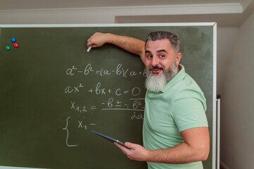 Teacher explaining mathematics on chalkboard holding tablet PC