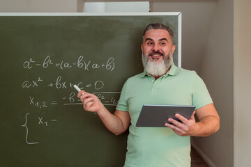 Mature teacher with tablet PC teaching mathematics on chalkboard