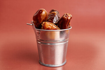 A small metal bucket filled with dried dates on a brown background.
