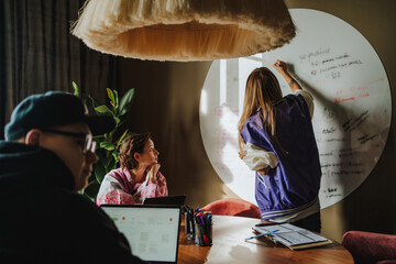 Musician writing on whiteboard in front of colleagues at desk