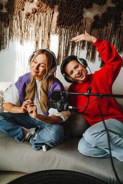 Happy musician recording podcast through microphone by colleague on sofa in studio