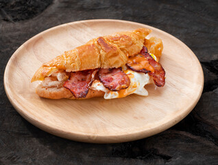 Croissant sandwich breakfast with egg and crispy bacon on plate.