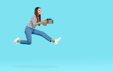 Fototapeta na wymiar Full body length side profile view happy cheerful joyful excited woman in casual jeans holding gift box, jumping high in air and flying on blue copy space background. Holiday sale and presents concept