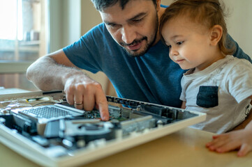 Cute boy looking at father repairing computer on table