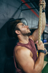 Obraz premium Vertical photo of a man climbing a rope in a gym