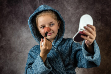 Fototapeta premium beautiful little girl trying to do her makeup in front of the mirror isolated