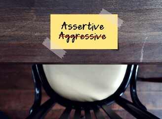Note stick on table with text written AGGRESSIVE, changed to ASSERTIVE , standing up for oneself...