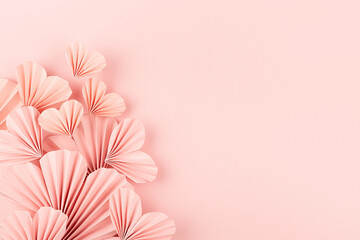 Valentines day background - pink paper ribbed hearts fly on soft light pastel pink background as sideways border with copy space, top view.