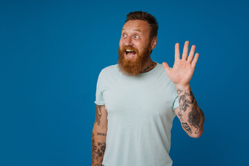 Ginger excited man with tattoo smiling and waving hand at camera