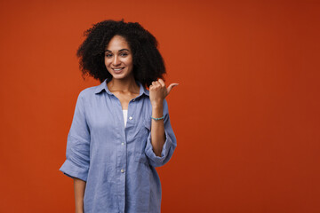 Young beautiful smiling curly woman pointing aside with thumb finger