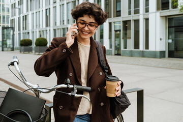 European woman talking on cellphone and drinking coffee at city street