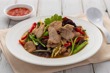 Stir-fried pork slices with shredded gingers and wood ear mushrooms, a simple Thai-Chinese food dish, served on a white serving plate with a small cup of chili-garlic relish as a side dish.