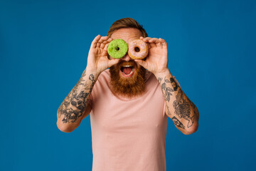 Bearded man holding donuts while standing isolated over blue background