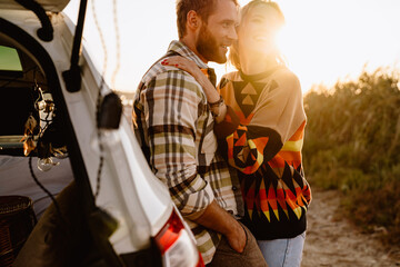 Happy young white couple standing by car while walking at seashore