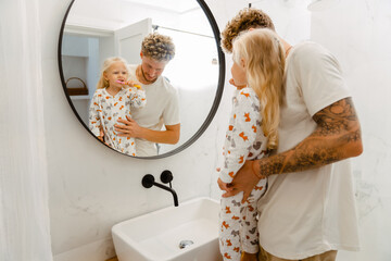Young father helping his little daughter to clean her teeth in bathroom