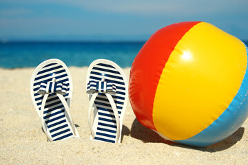 A Beach summer holiday banner background. Flip-flops and hat with a board and ball on the sand near the ocean. Summer accessories on the seashore. 