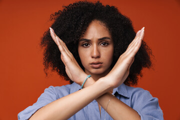 Displeased african woman holding hands crossed and looking at camera isolated