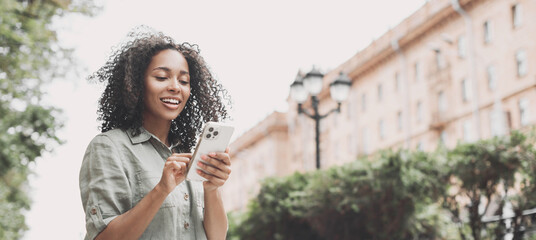 Young beautiful woman using smartphone in a city panoramic banner. Smiling student girl texting on mobile phone outdoor.  Modern lifestyle, connection, casual business concept - Powered by Adobe