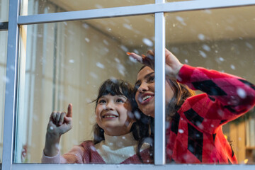 Adorable child looking at the window and admire snowflakes with mother. 