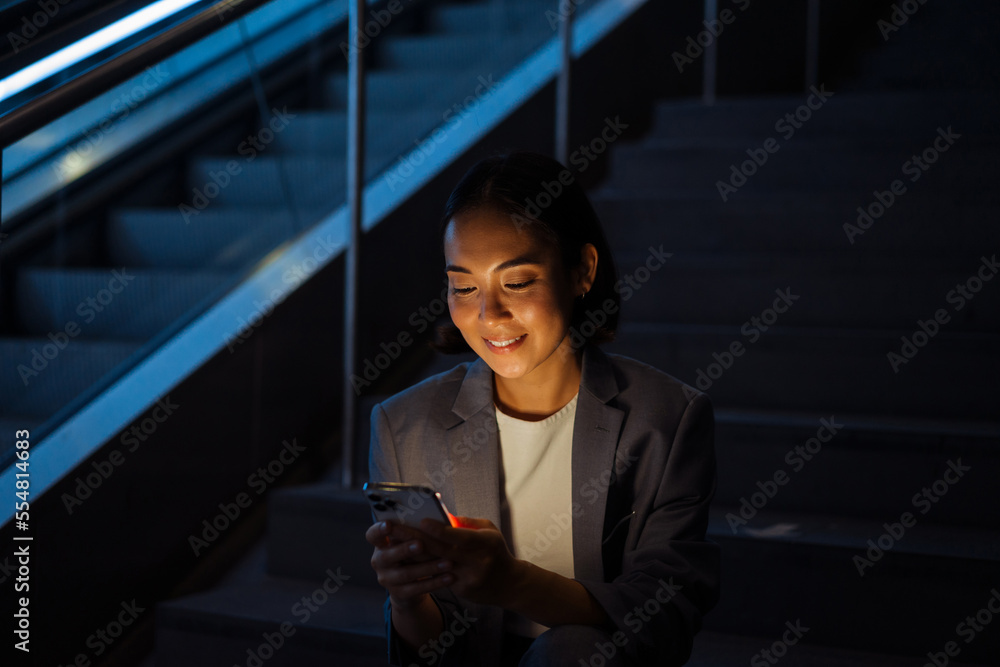 Wall mural young asian woman using mobile phone while sitting on stairs