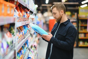 Young cheerful positive male customer making purchases in supermarket, buying household chemicals