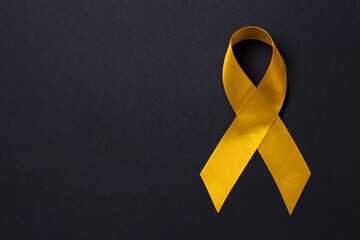 Gold ribbon close-up on a black background. Copy space. The concept of childhood cancer