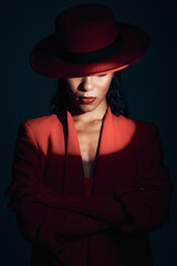 Fashion, red suit with spotlight for woman in dark, mystery and 90s retro on a black studio background. Designer, power and model with vintage clothes, arms crossed and makeup for empowerment