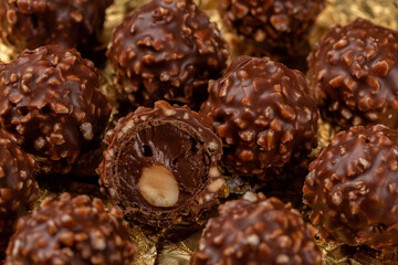 Chocolate and hazelnut ball candies. Whole roasted hazelnut  in a thin wafer shell filled with hazelnut chocolate, covered milk chocolate chopped hazelnuts. Confectionery on a gold wrapping foil.
