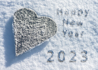vereistes Herz aus Eisen liegt im Schnee mit Schriftzug, Happy New Year 2023.