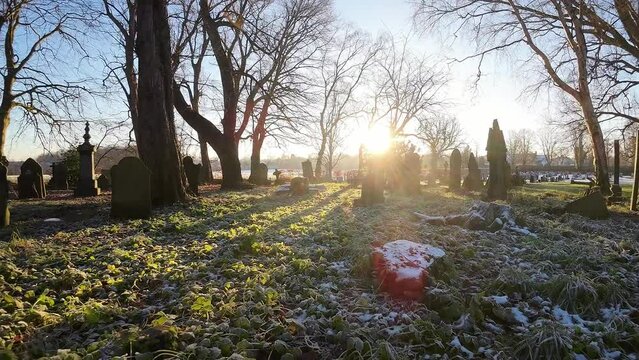 Flying FPV around headstones in snowy autumn sunrise churchyard cemetery during golden hour