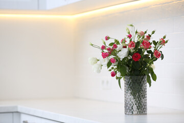 Vase with beautiful flowers on white countertop in kitchen, space for text