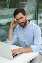Naklejka premium Portrait of handsome bearded man with laptop in outdoor cafe
