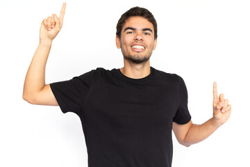 Excited young man pointing fingers up. Portrait of happy Caucasian male model with short dark hair in black T-shirt looking at camera, smiling, showing ads with fingers. Advertisement concept