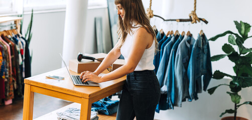 Young clothing store owner using a laptop in her shop