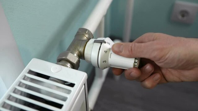 Man regulates the heat supply to a radiator with a thermostat knob. Hot pipes in winter. Increasing and decreasing the temperature in the system.