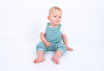 Close-up portrait of beautiful baby boy wearing light blue jumpsuit over white studio background smiling and looking aside. 