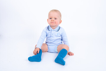Beautiful blond baby boy wearing blue sitting against white background and looking to the camera. 