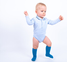 Beautiful blond baby boy wearing blue standing against white background smiling and looking to the camera. Baby taking his first steps. 